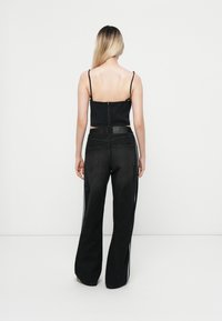 Svart croppad topp med tunna band, dragkedja i ryggen; tillsammans med högmidjade svarta jeans som har vita sidostråkar och vida ben.