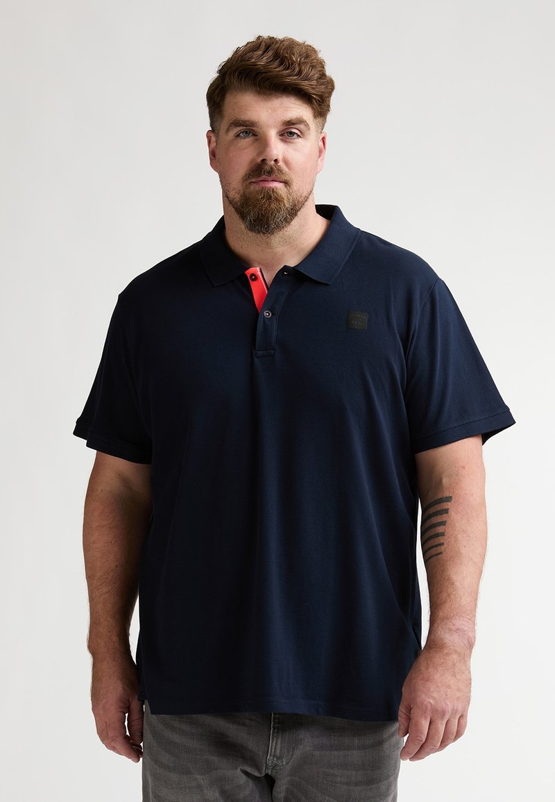 Polo à manches courtes bleu marine avec un accent de col corail, col traditionnel et patch logo sur la poitrine gauche. Matière en mélange de coton.