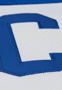 Un tessuto bianco con una grande lettera "C" ricamata in blu. La cucitura è liscia con una leggera lucentezza, che mette in risalto la forma della lettera.