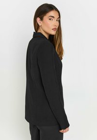 Svart kavaj med en figursydd design, revere och två framfickor. Slät tyg med en subtil lyster och skräddarsydd silhuett.