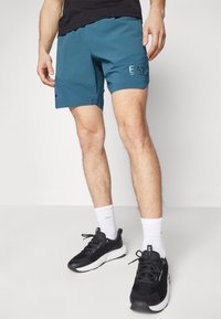 Turkosa träningsshorts med ett rutmönster, elastisk midja och detaljer i svart logotyp. Bärs med svarta sneakers och vita strumpor.