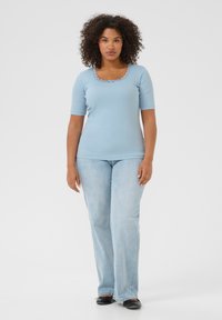 Light blue ribbed short-sleeve top with a scalloped lace neckline, paired with light blue flared jeans and black flats.