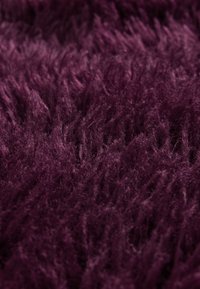 Lila Shag-Teppich mit einer hochflorigen Struktur, der dichte und flauschige Fasern aufweist und eine weiche, fühlbare Oberfläche schafft.