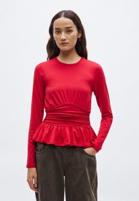 Rød genser med lange ermer, drapert overdel, peplumkant og rund hals. Laget av mykt stoff, kombinert med bukser med avslappet passform.