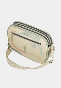 Bolso cruzado beige con tres compartimentos con cremallera, detalles verdes y patrones abstractos en tonos pasteles. Incluye correa ajustable.