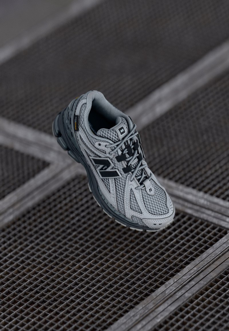 Harmaa juoksukenkaat, joissa on verkkomateriaalista päällinen, mustat yksityiskohdat, pehmustettu kaulus ja teksturoitu pohja, jossa on korostettu pito. Varustettu nauhoitusjärjestelmällä tukevan istuvuuden saavuttamiseksi.