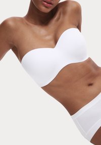Witte strapless beha met een gladde, gevormde ontwerp. Heeft een gegolfde rand en naadloze textuur. Gecombineerd met een witte slip.