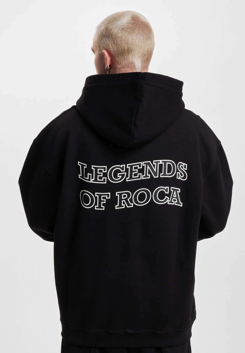 Fekete kapucnis pulóver, hátul nagy fehér szöveggel: „LEGENDS OF ROCA”. Relaxált szabású, bordás mandzsettákkal és aljjal rendelkezik.