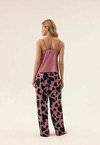Różowa satynowa kamizelka na cienkich ramiączkach, połączona z luźnymi różowymi spodniami z dużymi czarnymi wzorami w kształcie serca. Teksturowany materiał i swobodny krój.