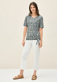 Top de manga corta en verde oscuro con patrón geométrico blanco, combinado con pantalones cortos blancos y sandalias marrones. El material parece ligero.