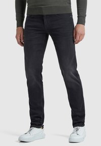 Temno sivi kavbojke iz denima, slim fit dizajn, z sprednjimi žepi, v kombinaciji z belimi supergami. Poudarjen pogled na spodnji del telesa.