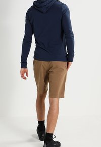 Granatowa bluza z kapturem z długim rękawem i khaki szorty. Szorty mają prosty krój i sięgają do kolan, zestawione z czarnymi butami sportowymi i skarpetkami.