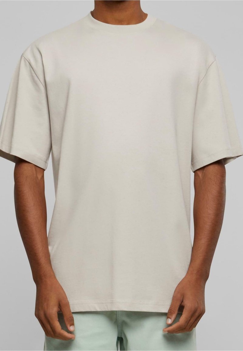 T-shirt en coton beige oversize avec col rond, épaules tombantes et manches courtes. Texture lisse, détails de couture minimaux.
