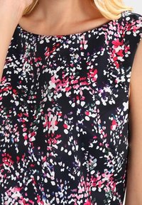 Robe sans manches en tissu noir ornée d'un motif abstrait coloré de taches roses, blanches et violettes, avec un col bateau.