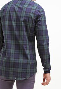 Långärmad rutig skjorta i nyanser av lila och grön, med knäppning vid ärmslut och en krökt nederdel. Slät tyg med en kroppsnära design.