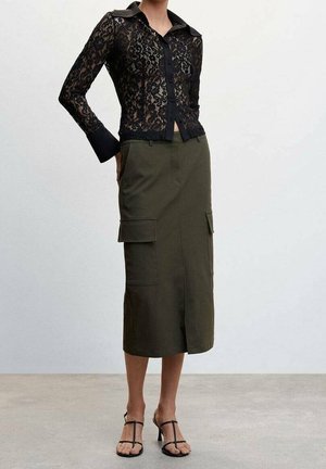 Černá krajková halenka s dlouhými rukávy a límečkem, doplněná olivově zelenou cargo sukní s kapsami, nošená s černými sandály na pásky.