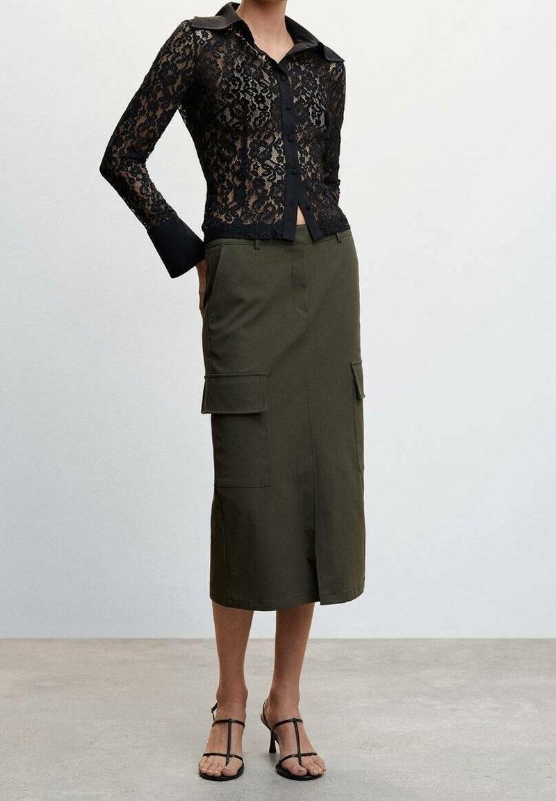 Blouse en dentelle noire à manches longues et col, associée à une jupe cargo vert olive avec poches, portée avec des sandales noires à lanières.