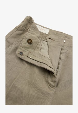 Cintura beige dei pantaloni con cerniera parzialmente aperta, bottone di chiusura e etichetta del marchio "Slowear Incotex" all’interno.