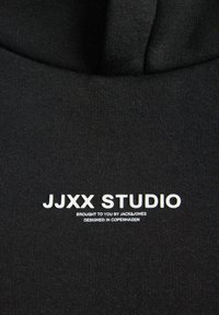 Gros plan sur un tissu noir avec texte blanc "JJXX STUDIO brought to you by Jack & Jones designed in Copenhagen."