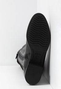 Botín de cuero negro con un upper texturizado, cremallera lateral y suela de goma negra con un patrón de olas y el logotipo de la marca.