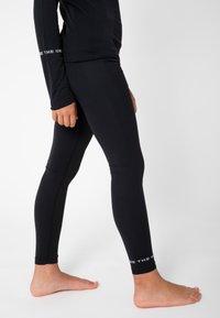 Schwarze Sportleggings mit körperbetontem Design, dehnbarem Material, strukturierten Akzenten an den Knien und einem bedruckten Logo nahe dem Knöchel.