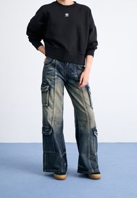 Svart sweatshirt med en liten vit logotyp, kombinerad med lösa, urblekta blå denim-cargobyxor med flera fickor och en bred ben design.