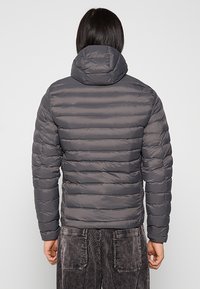 Grå dunjakke med vandrette stikninger, hætte og elastiske manchetter. Fremstillet af et glat, vandafvisende materiale, der giver isolering.