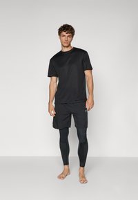 Svart tränings t-shirt kombinerad med svarta shorts och svarta kompressionsbyxor. Enkla linjer, slät struktur och inga synliga mönster.