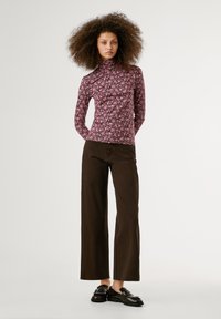 Langarmige turtleneck in roze met een bloemenpatroon, gecombineerd met hooggerite bruine wijde broek en zwarte instappers met zilveren accenten.