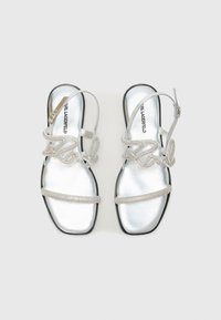 Silver flat sandals feature a metallic surface, delicate beaded straps with a scripted "love" design, and a black rubber sole.