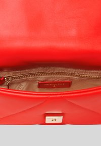 Borsa a tracolla rossa in pelle con design trapuntato, dotata di una chiusura in tonalità oro e un interno beige con tasca con zip e etichetta del marchio.