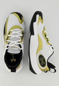 Sneakers bianchi e neri con accenti gialli, tomaia in rete testurizzata, forma arrotondata e suola in gomma con un logo sul lato.
