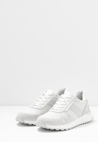Bílé tenisky s kombinací hladkých a texturovaných materiálů, šněrovacím designem a jemnými perforacemi na boku.