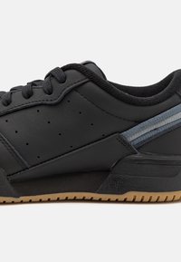 Svart syntetisk lädersneaker med en texturerad svart sula, perforerad detaljering och ett blått ackentskikte på sidan.