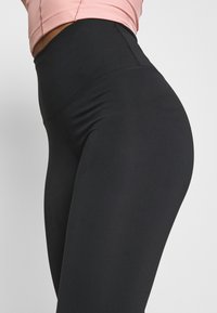 Leggings noirs taille haute en tissu lisse et extensible, avec des coutures plates pour le confort et une silhouette ajustée.