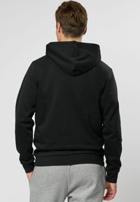 Zwarte capuchontrui met een gladde textuur, geribde manchetten en onderrand, en een kangoeroezak. Draagt met grijze trainingsbroek.