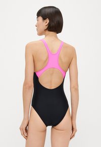 Μαύρο μαγιό με ροζ σχεδιασμό στον αγκώνα με αγωνιστική πλάτη, που διαθέτει άνοιγμα στην πλάτη. Ομαλή υφή και μινιμαλιστικό στυλ κατάλληλο για κολύμβηση.