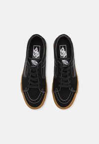 Baskets en toile noires avec des coutures blanches, des lacets noirs et une semelle en caoutchouc gum. Design bas classique. Logo Vans sur la languette.