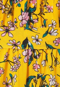 Blumenerstoff mit bunten Blumen in Pink, Weiß und Grün auf einem gelben Hintergrund mit plissiertem Muster.
