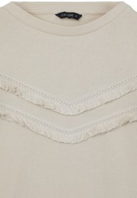 Felpa beige con scollo rotondo, caratterizzata da due dettagli a V sovrapposti con frange lungo il petto. Tessuto morbido e textured.