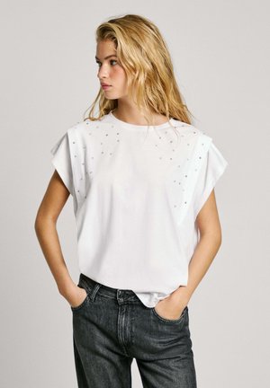 Hvid bomulds T-shirt med korte, rullede ærmer, udsmykket med små nitter ved skuldrene, parret med mørke denim jeans.
