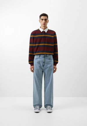 Striped long-sleeve polo shirt in burgundy, yellow, and green; white collar. Light blue baggy jeans. White sneakers with blue accents.