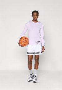 Μωβ πουκάμισο με μακριά μανίκια και λευκή βερμούδα μπάσκετ με μαύρες ρίγες, κρατώντας μια μπάλα μπάσκετ. Γκρι κάλτσες και μαύρα αθλητικά παπούτσια συμπληρώνουν την εμφάνιση.