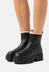 Bottines en cuir noir avec une finition texturée, dotées d'un col en fausse fourrure et de semelles en caoutchouc épaisses et crantées.