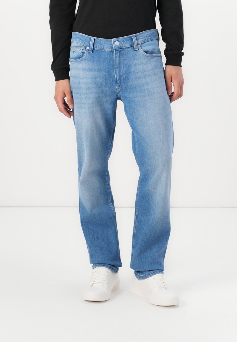 Jean droit bleu clair en denim, avec un design classique à cinq poches et un léger délavage. Assorti avec des baskets blanches.