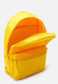 Zaino giallo con un tessuto testurizzato, dotato di un vano principale con zip e una tasca frontale, entrambi con zip lisce e un rivestimento brillante.