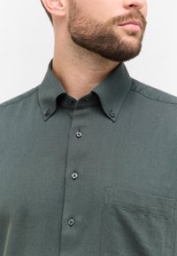 Groen hemd met een visgraatpatroon en een button-down kraag, voorzien van donkere knopen en een borstzak, gemaakt van structurele stof.