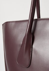 Bordeaux leren tote bag met een gladde textuur, stevige handvatten en nette stiksels. Heeft een minimalistisch ontwerp zonder zichtbare hardware.