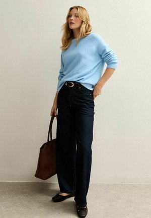 Lichtblauwe gebreide trui met een relaxed fit, gecombineerd met donkerblauwe wijde jeans. Een bruine totebag en zwarte ballerina's maken de look compleet.