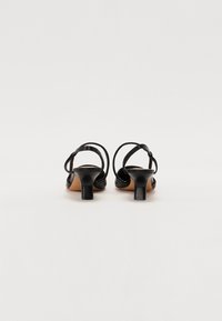 Sandales à talons hauts noires à lanières, avec un design à bout ouvert, en cuir lisse et un talon épais pour plus de stabilité.